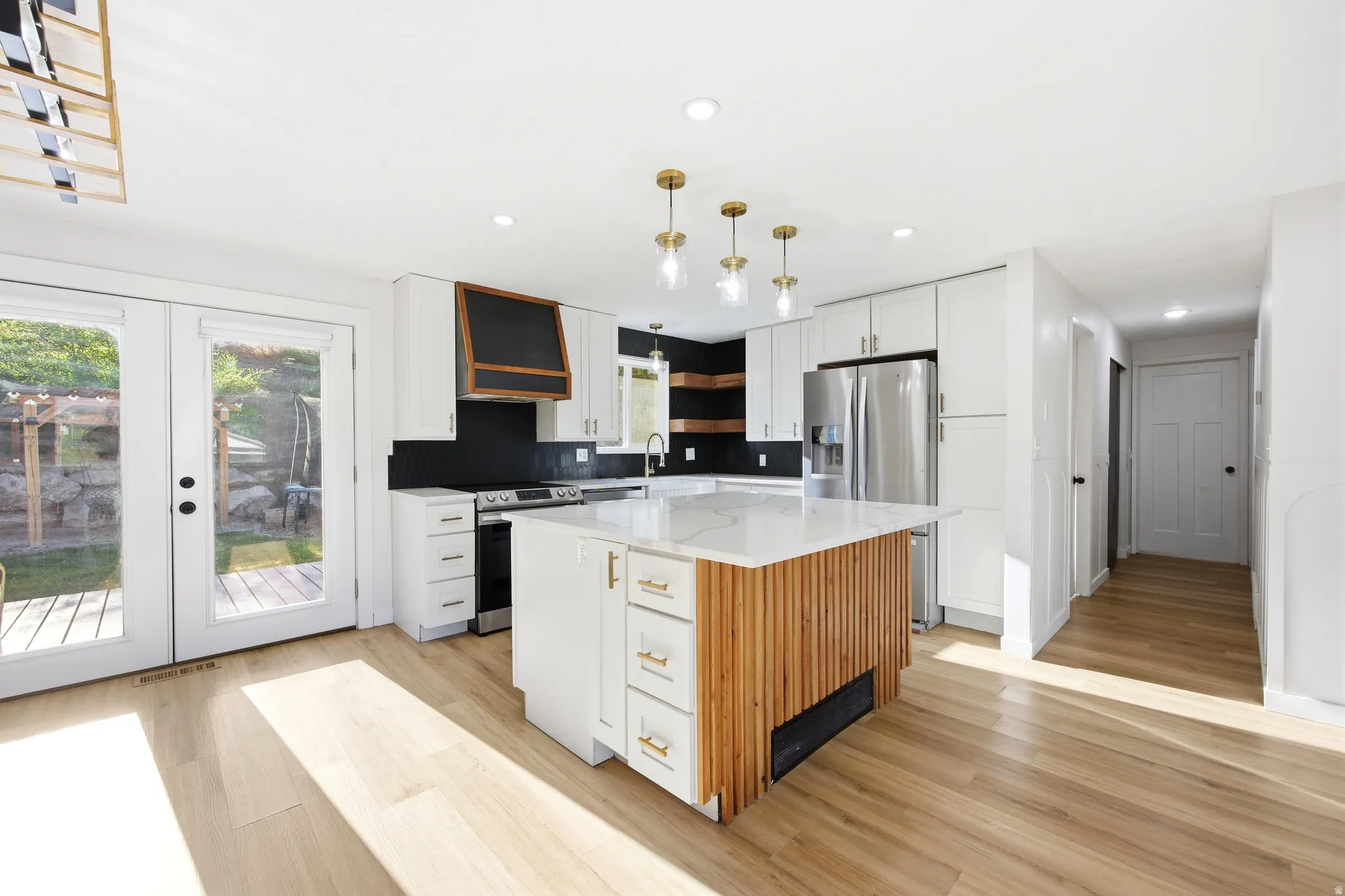 Open-concept kitchen featuring a central island with a slatted wood-finish base, white cabinetry, a black tile backsplash, and light wood-finish flooring