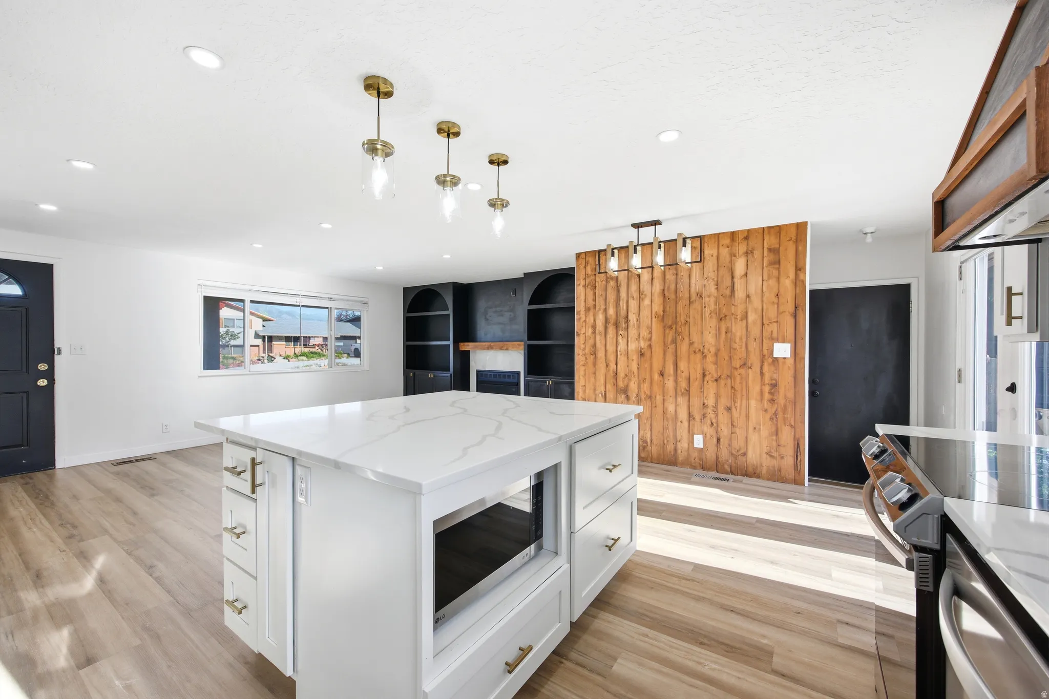 Open-concept living space featuring a white kitchen island with a quartz countertop, recessed lighting, wood-finish flooring, a wood accent wall, and built-in shelving with a fireplace
