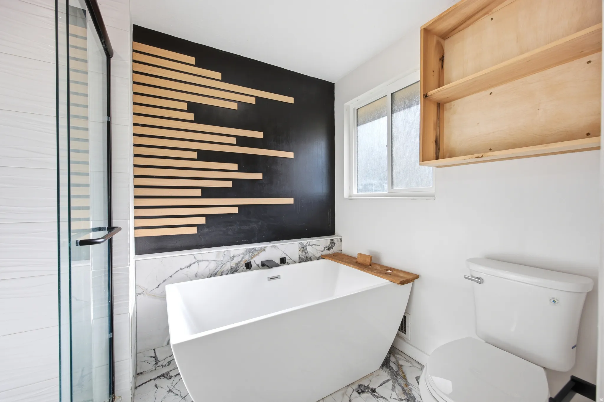 Modern bathroom featuring a freestanding soaking tub, marble-look tile flooring and wainscoting, and a glass-enclosed shower with white tiled walls