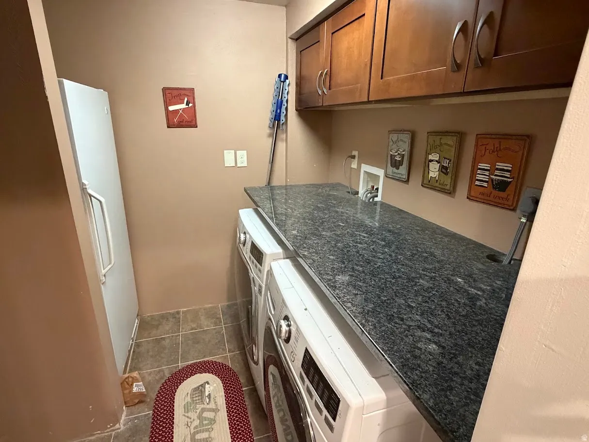 Laundry area featuring washer / dryer, cabinet space, and dark tile patterned flooring