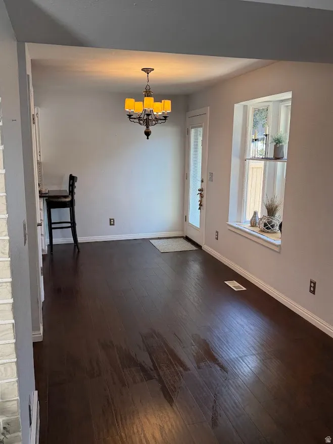 Spacious room featuring dark wood-finish flooring, a decorative chandelier, and a bay window with a deep sill
