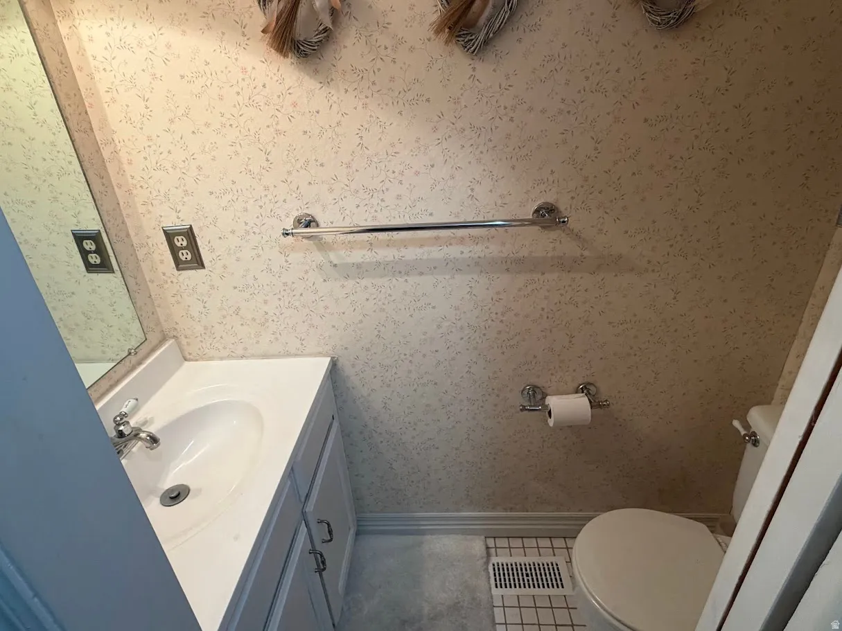 Half bathroom with vanity, wallpapered walls, and light tile patterned floors