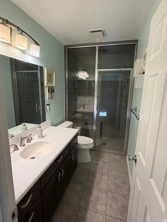 Full bath with vanity, a stall shower, a textured wall, and light tile patterned floors