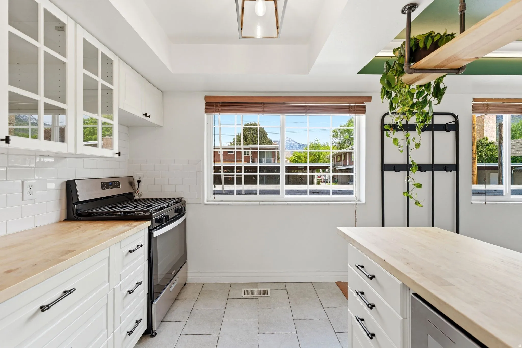 Kitchen featuring butcher block counters, white cabinets, glass fronted cabinets, stainless steel gas stove, and a raised ceiling