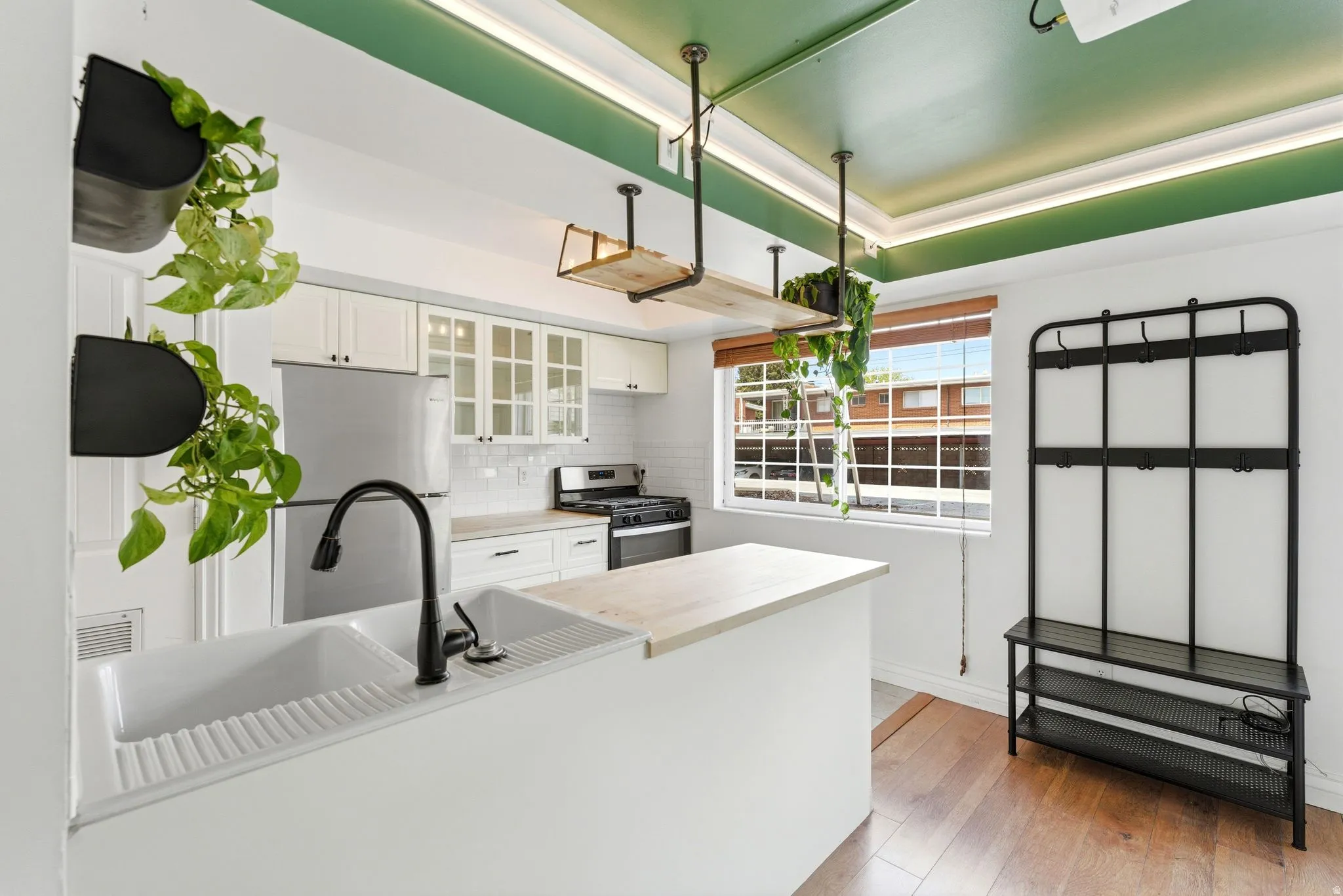 Kitchen with white cabinets, stainless steel appliances, light countertops, decorative backsplash, and light wood-style flooring