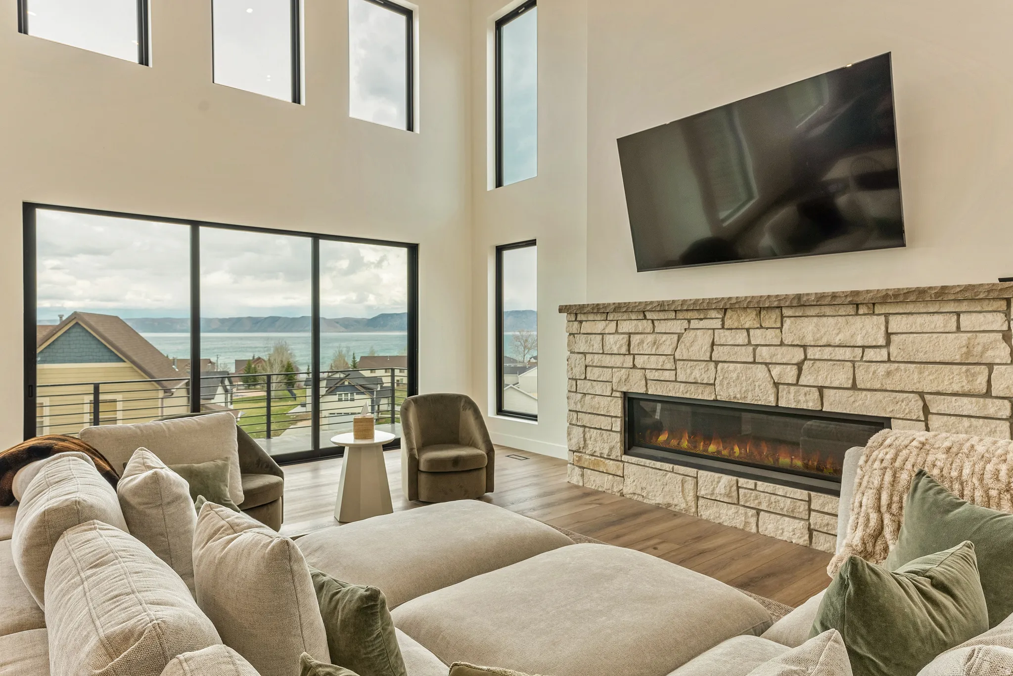 Living room featuring a stone fireplace, wood finished floors, plenty of natural light, and a high ceiling