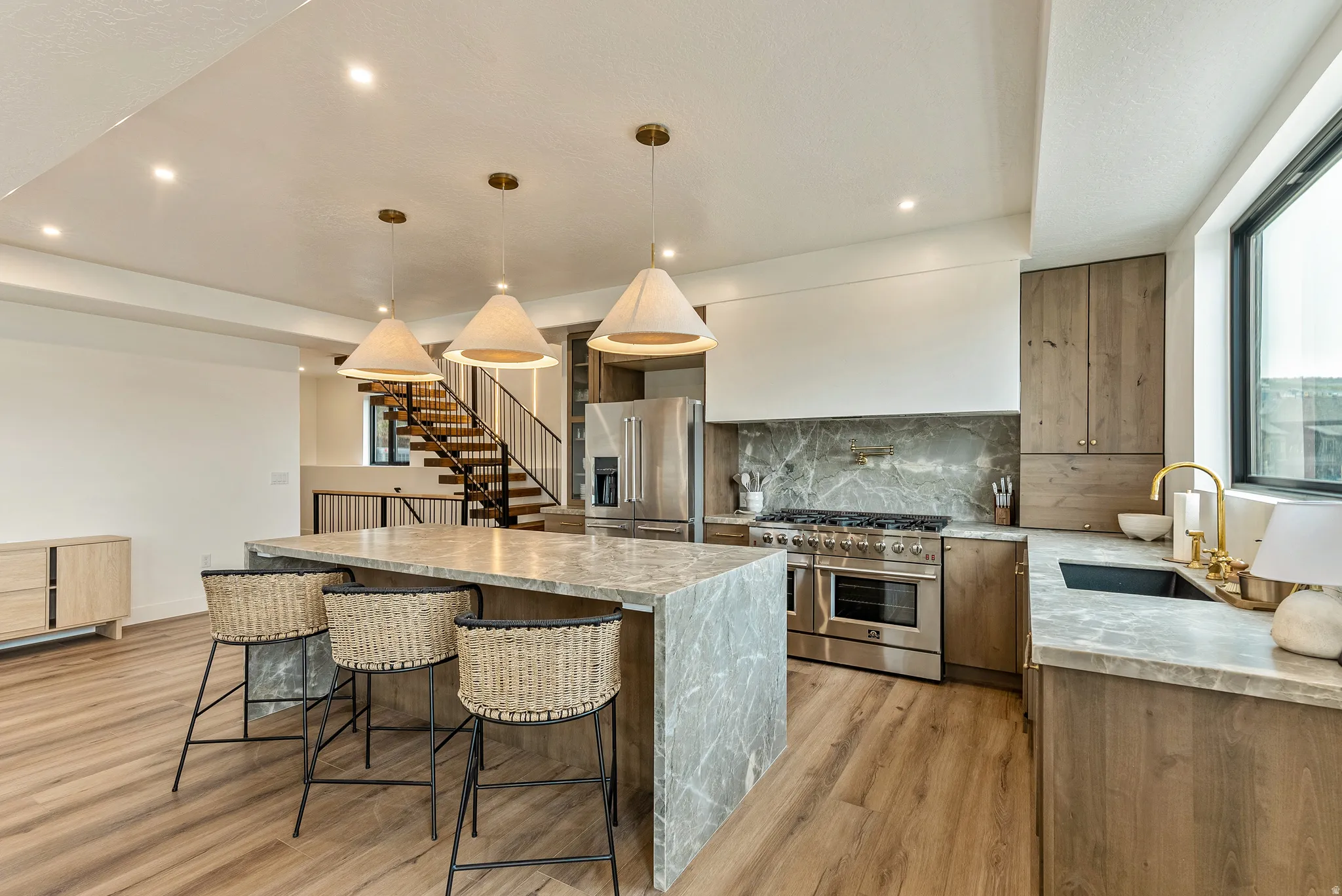 Kitchen featuring light stone countertops, high quality appliances, tasteful backsplash, light wood-type flooring, and pendant lighting
