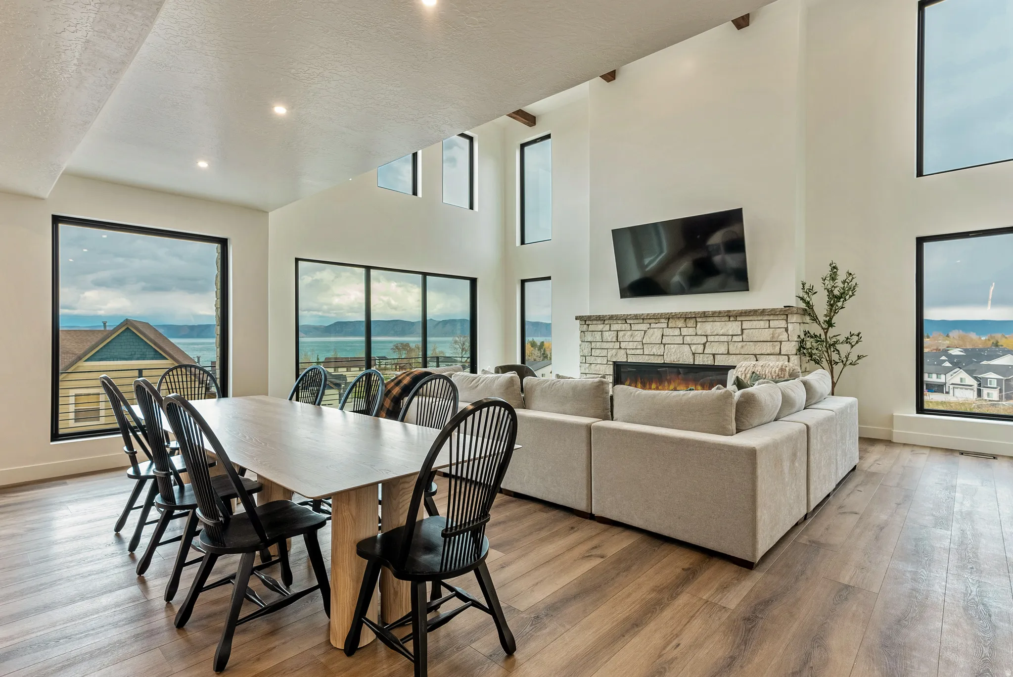 Dining area with light wood finished floors, a high textured ceiling, a stone fireplace, and recessed lighting
