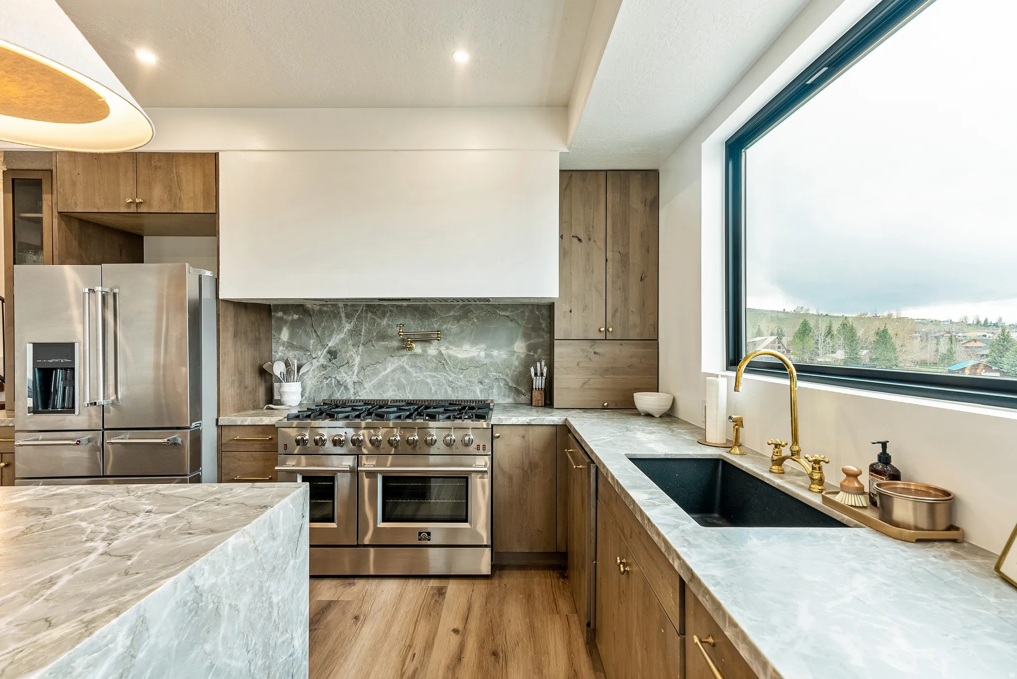 Kitchen with wood finish cabinetry, high quality appliances, light stone counters, light wood-style floors, and recessed lighting