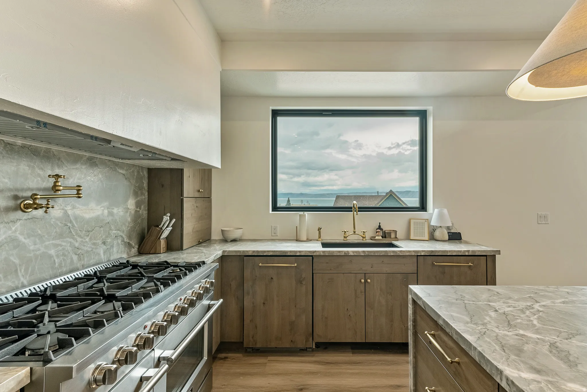 Kitchen with range with two ovens, backsplash, light wood-style floors, dishwasher, and light stone countertops