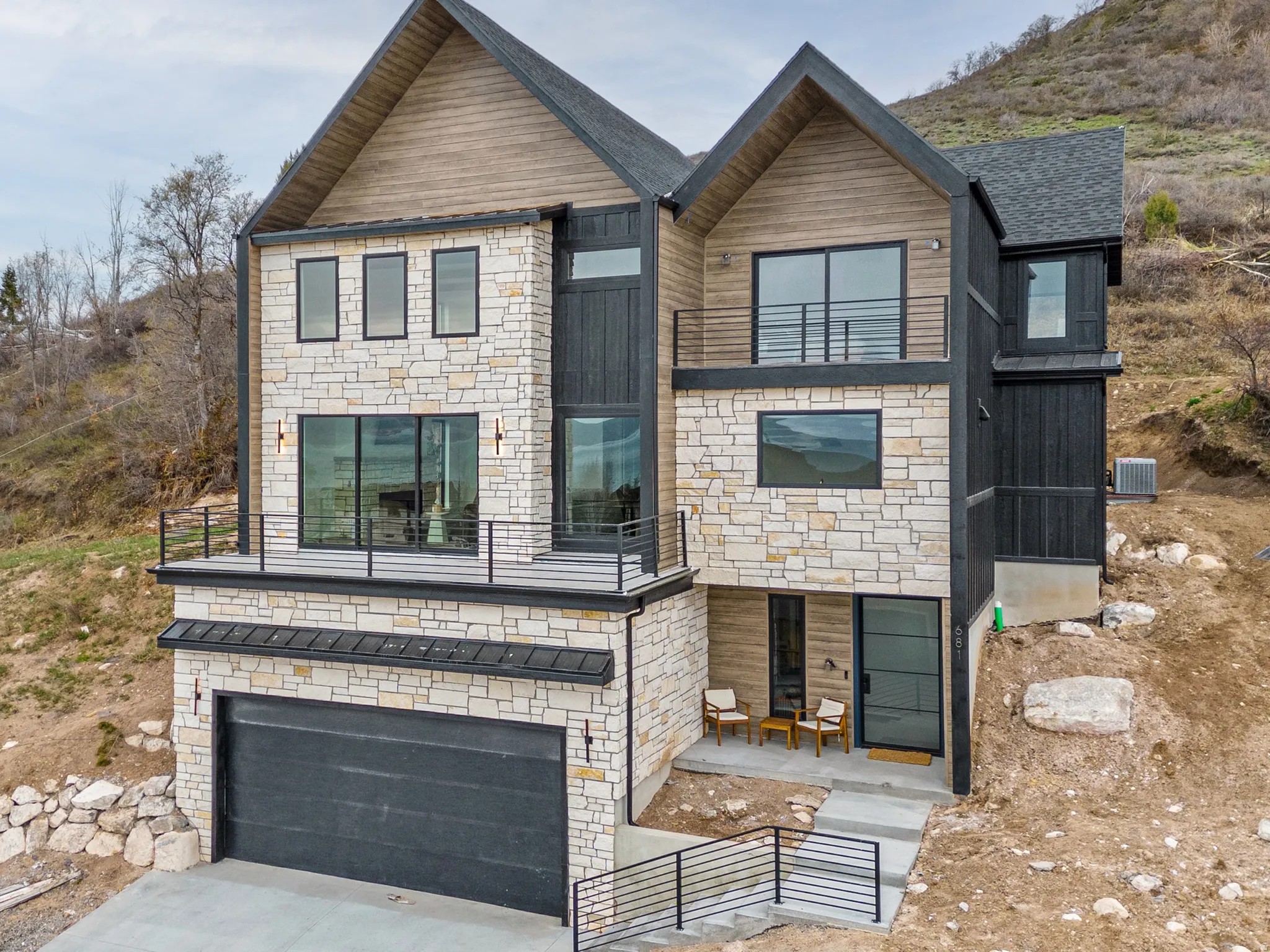 Modern home with stone siding, a garage, concrete driveway, and a balcony