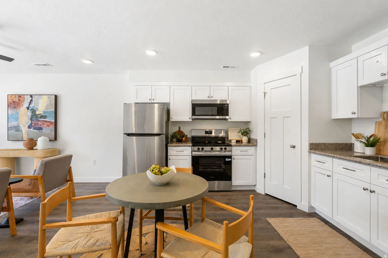 Kitchen with stainless steel appliances, dark stone counters, white cabinets, dark wood finished floors, and recessed lighting