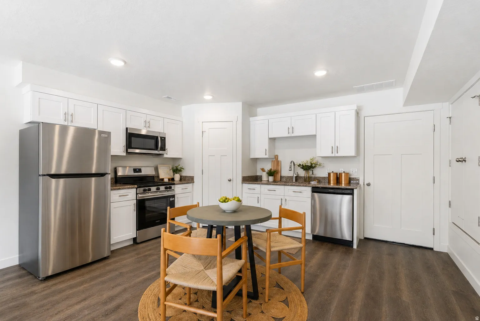 Kitchen featuring stainless steel appliances, white cabinetry, dark wood-style flooring, dark stone counters, and recessed lighting