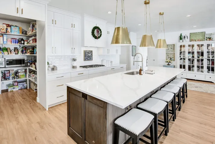 Dual tone kitchen with a breakfast bar area, light stone countertops, a spacious island, two tone cabinetry, and light wood-style floors
