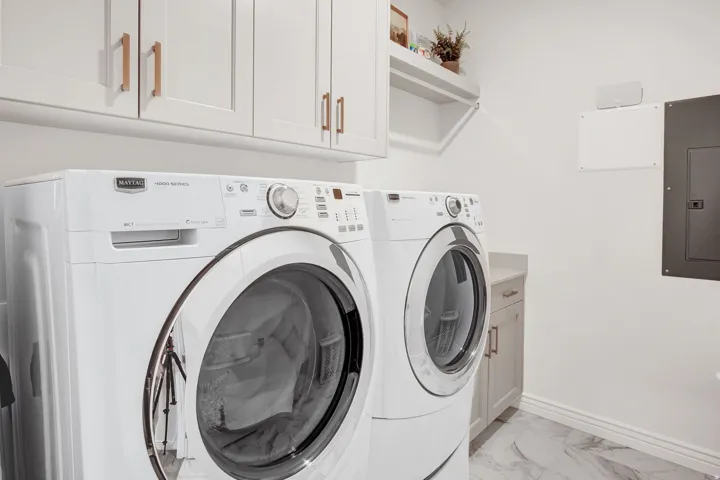 Laundry room featuring electric panel, washing machine and clothes dryer, cabinet space, and light marble finish flooring