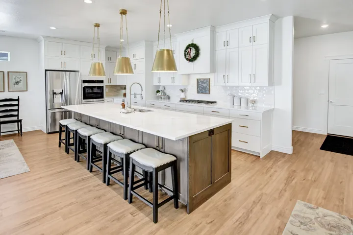 Two tone kitchen with two tone cabinets, stainless steel appliances, a large island with sink, light wood finished floors, and light stone countertops