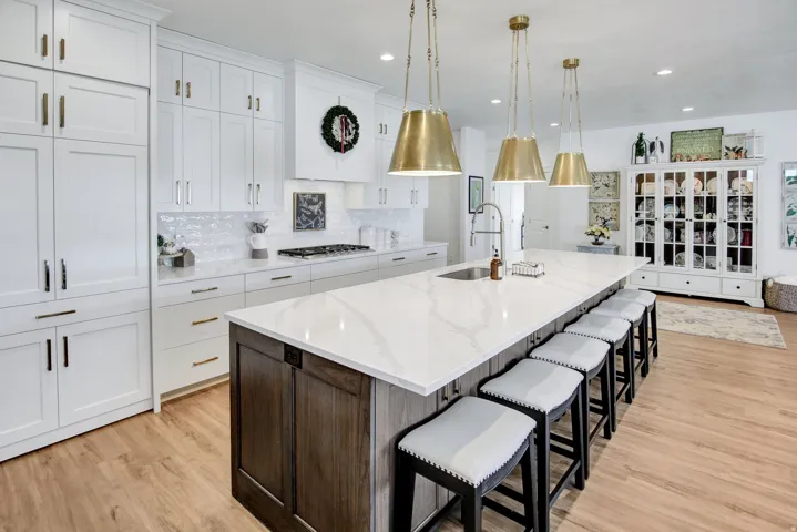 Two tone kitchen featuring a kitchen breakfast bar, two tone cabinetry, light stone countertops, a large island, and light wood-style floors