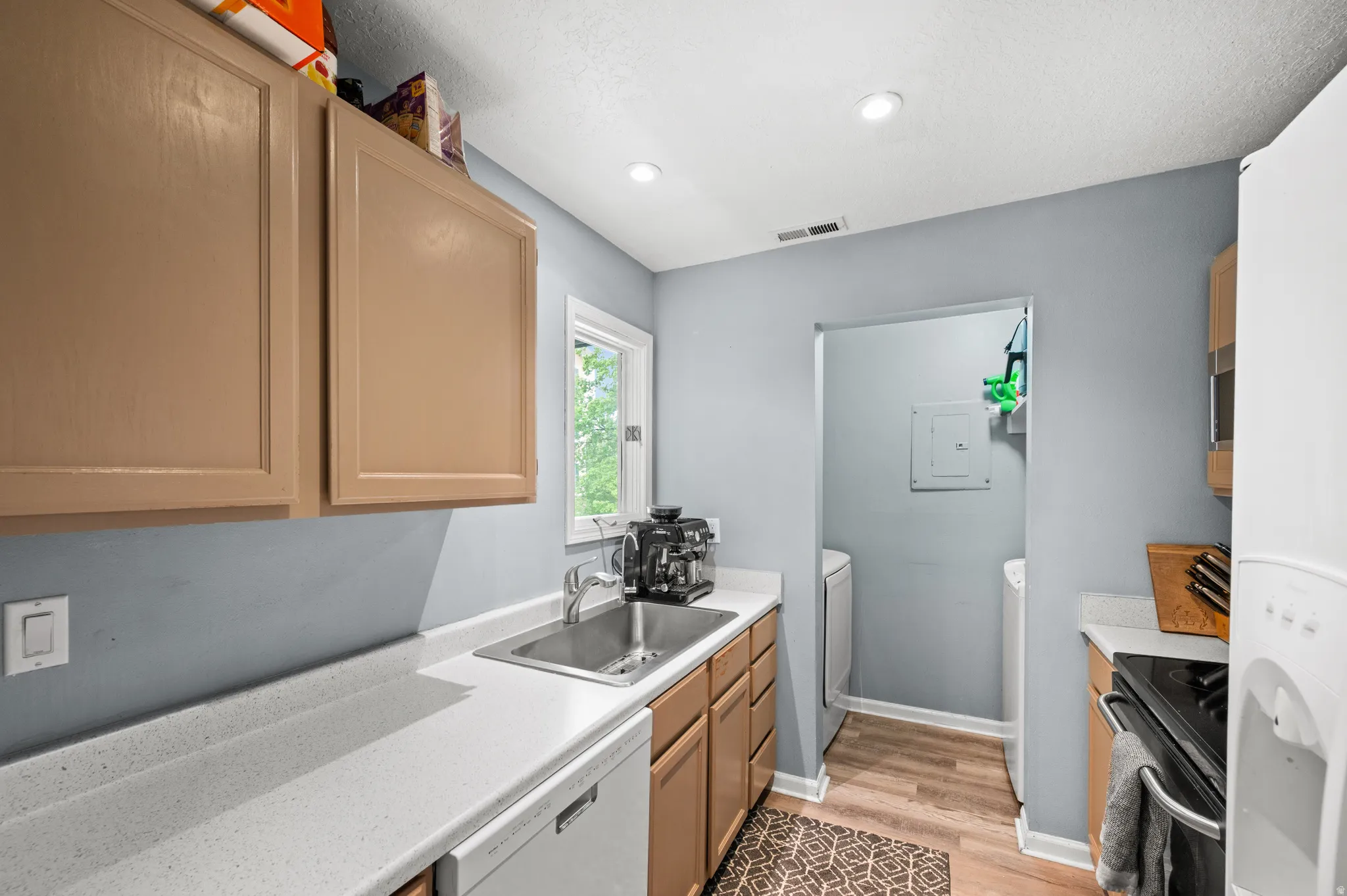 Kitchen with light countertops, white  and stainless steel appliances, electric panel, light wood-type flooring, and washer/dryer included