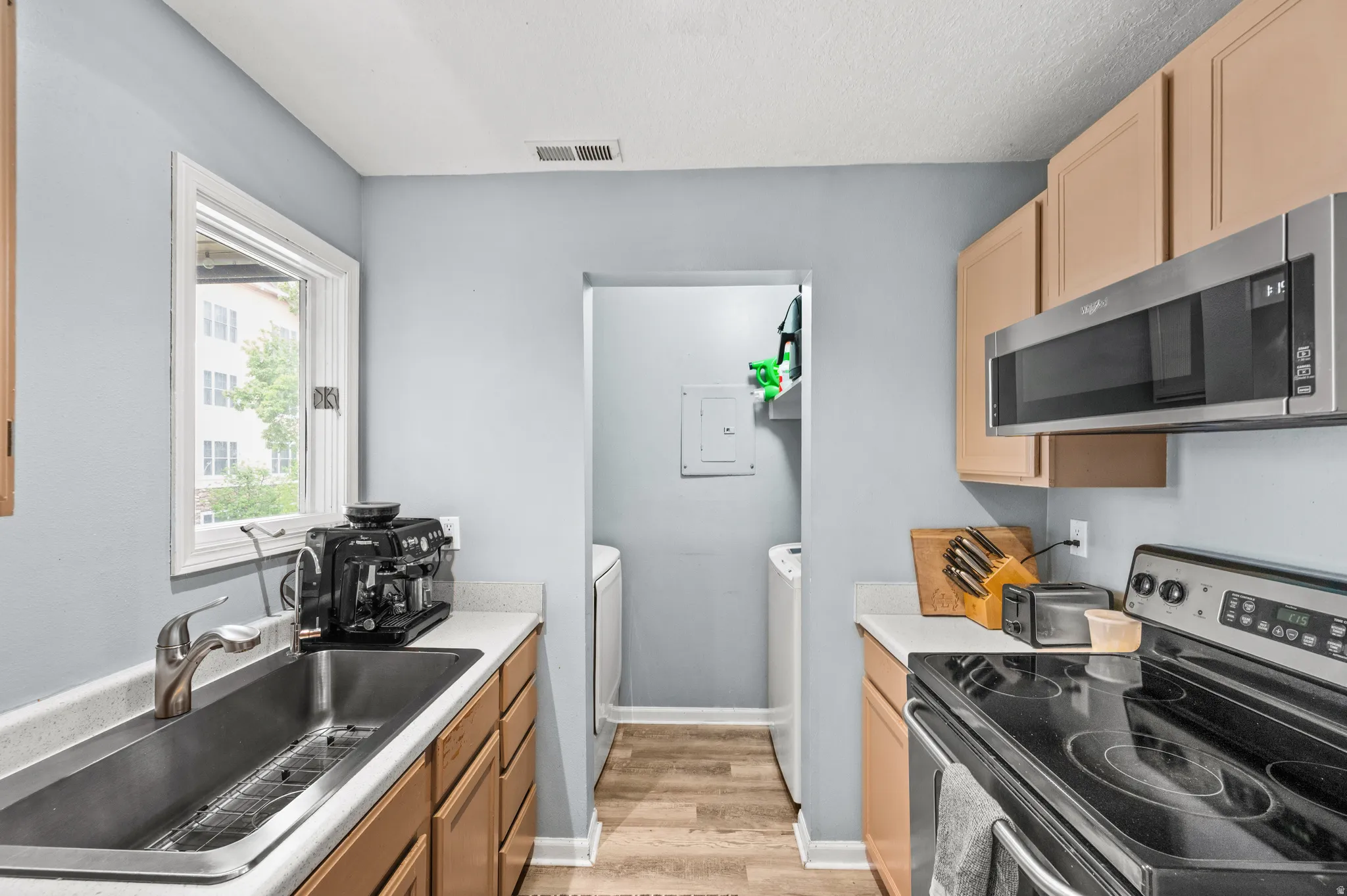 Kitchen with white and stainless steel appliances, light countertops, washer/dryer tucked away, and light wood finish cabinets