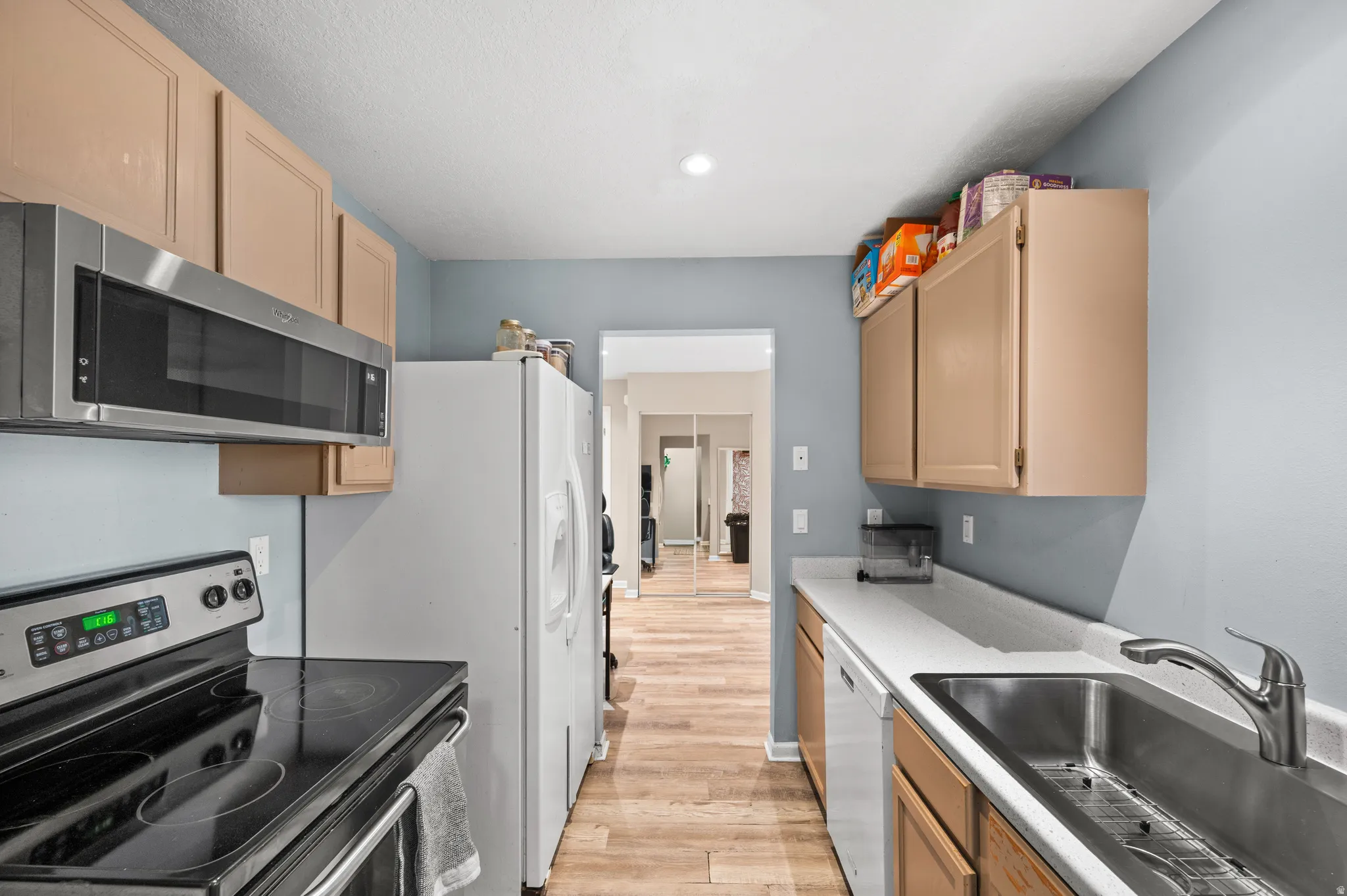 Kitchen with white and stainless steel appliances, light wood finish cabinetry, light wood-type flooring, and light countertops