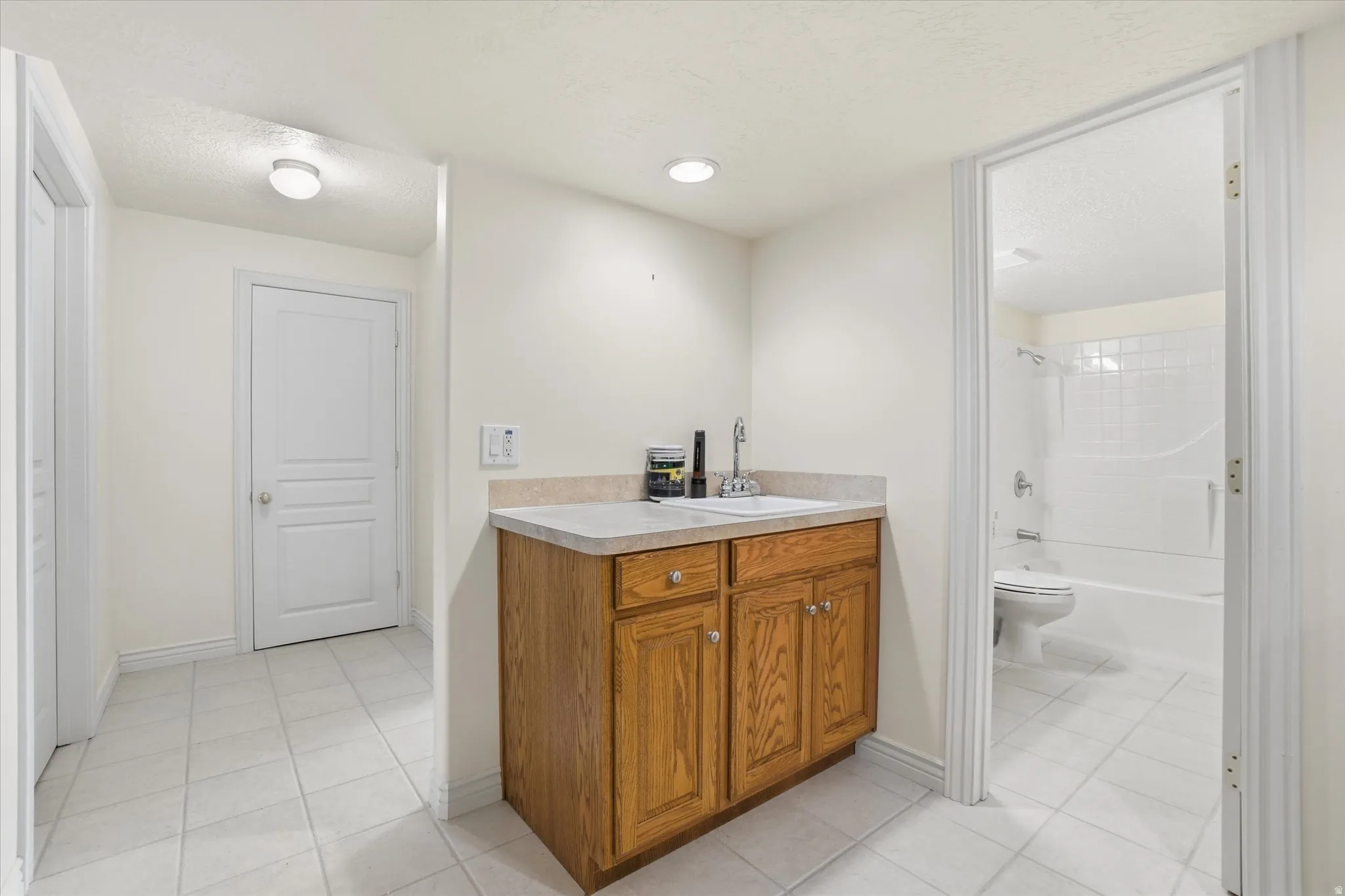 Utility area featuring a wood-finish cabinet with a sink, light-toned countertop, and recessed lighting