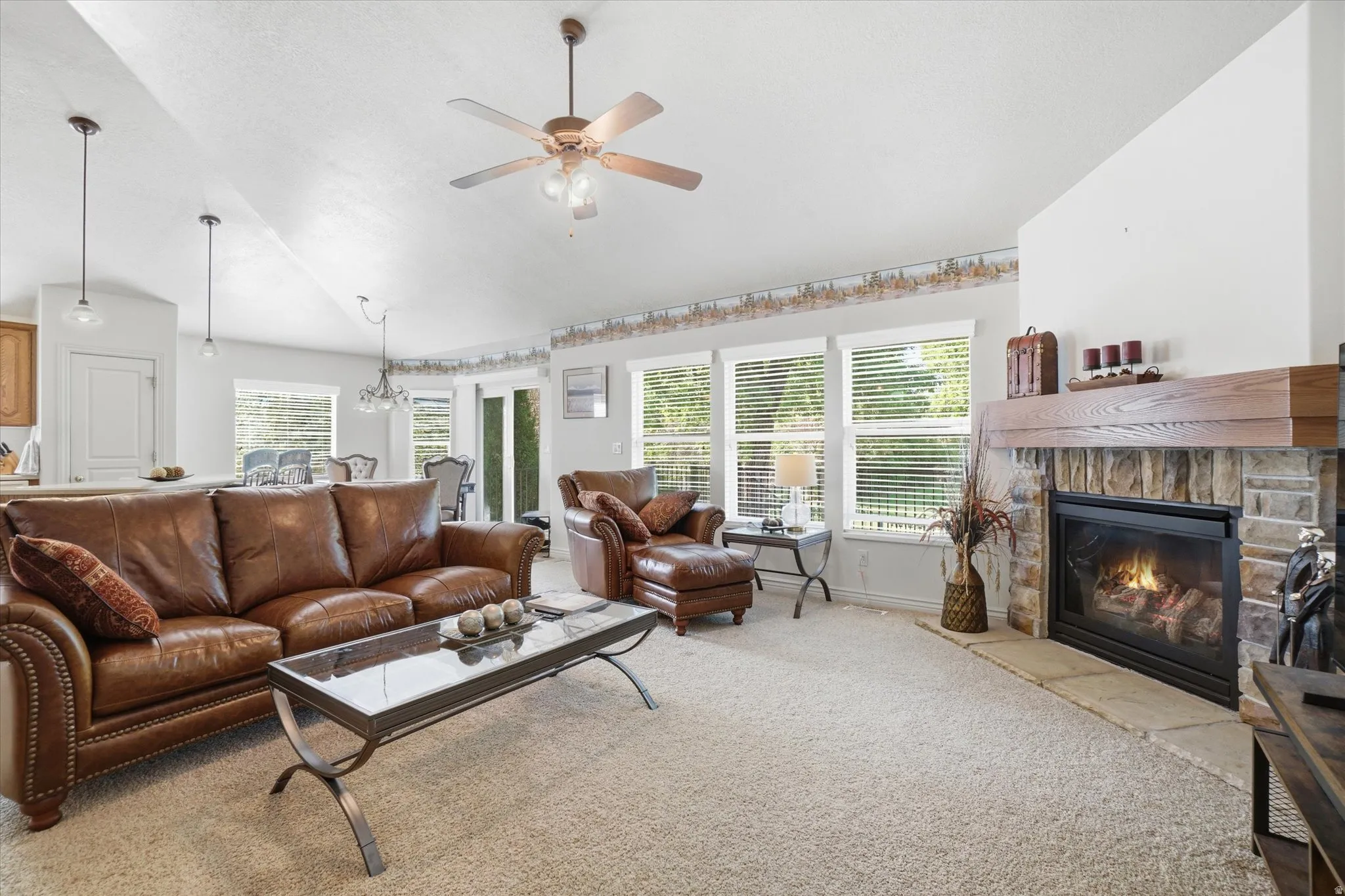 Living area featuring a stone fireplace with a wood-beam mantel, vaulted ceilings, and a ceiling fan
