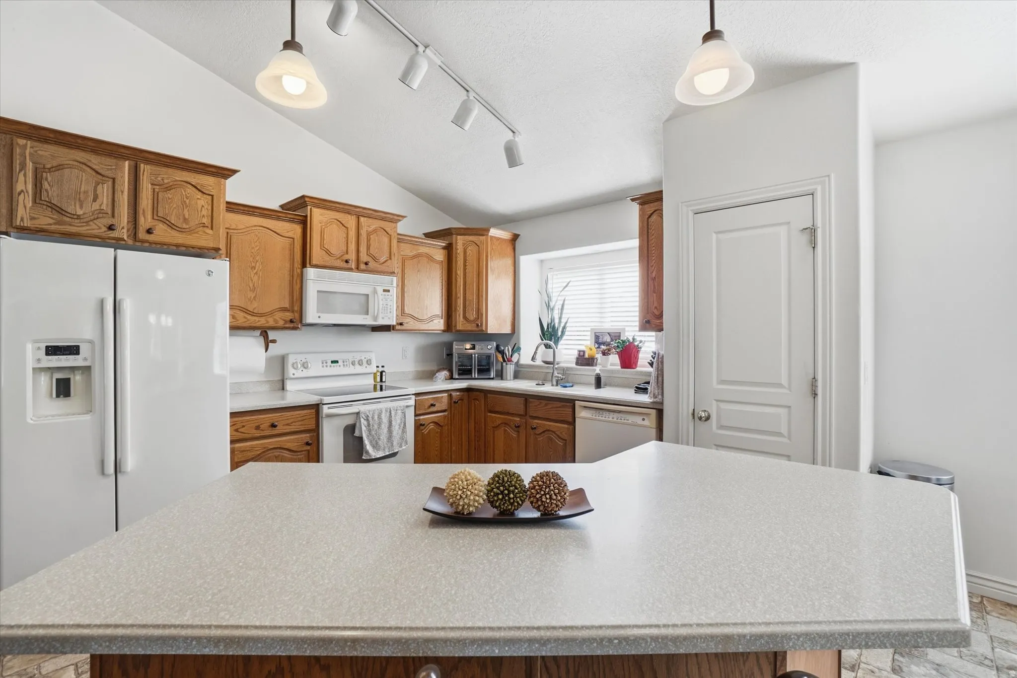 Kitchen featuring a peninsula with a light-toned countertop, wood cabinetry, vaulted ceilings, track lighting, and a window with horizontal blinds