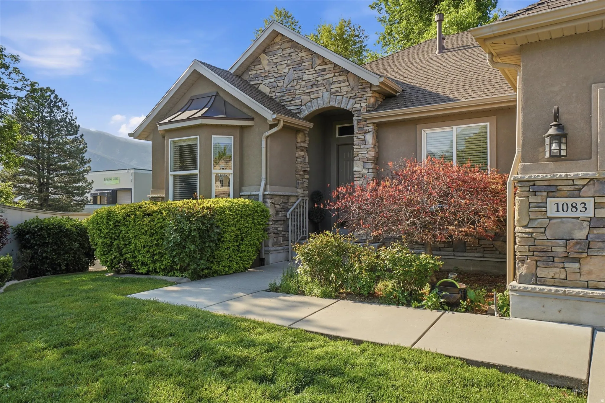 Stone and stucco exterior featuring a bay window with copper-finish roofing, an arched entryway, and an outdoor wall lantern