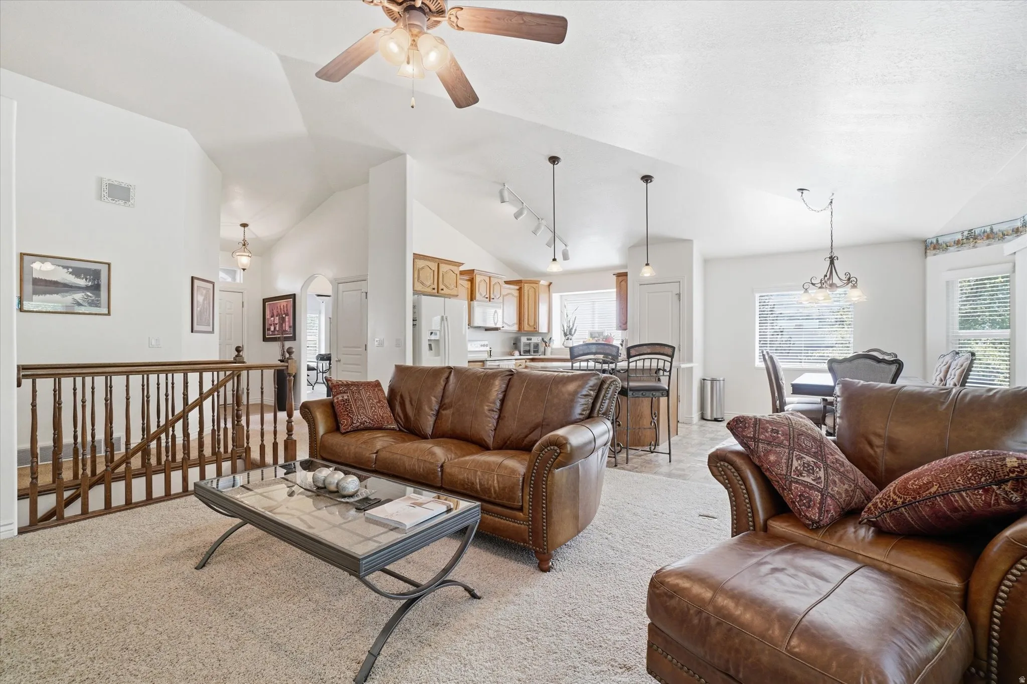 Spacious living area featuring vaulted ceilings, a ceiling fan, and carpet flooring