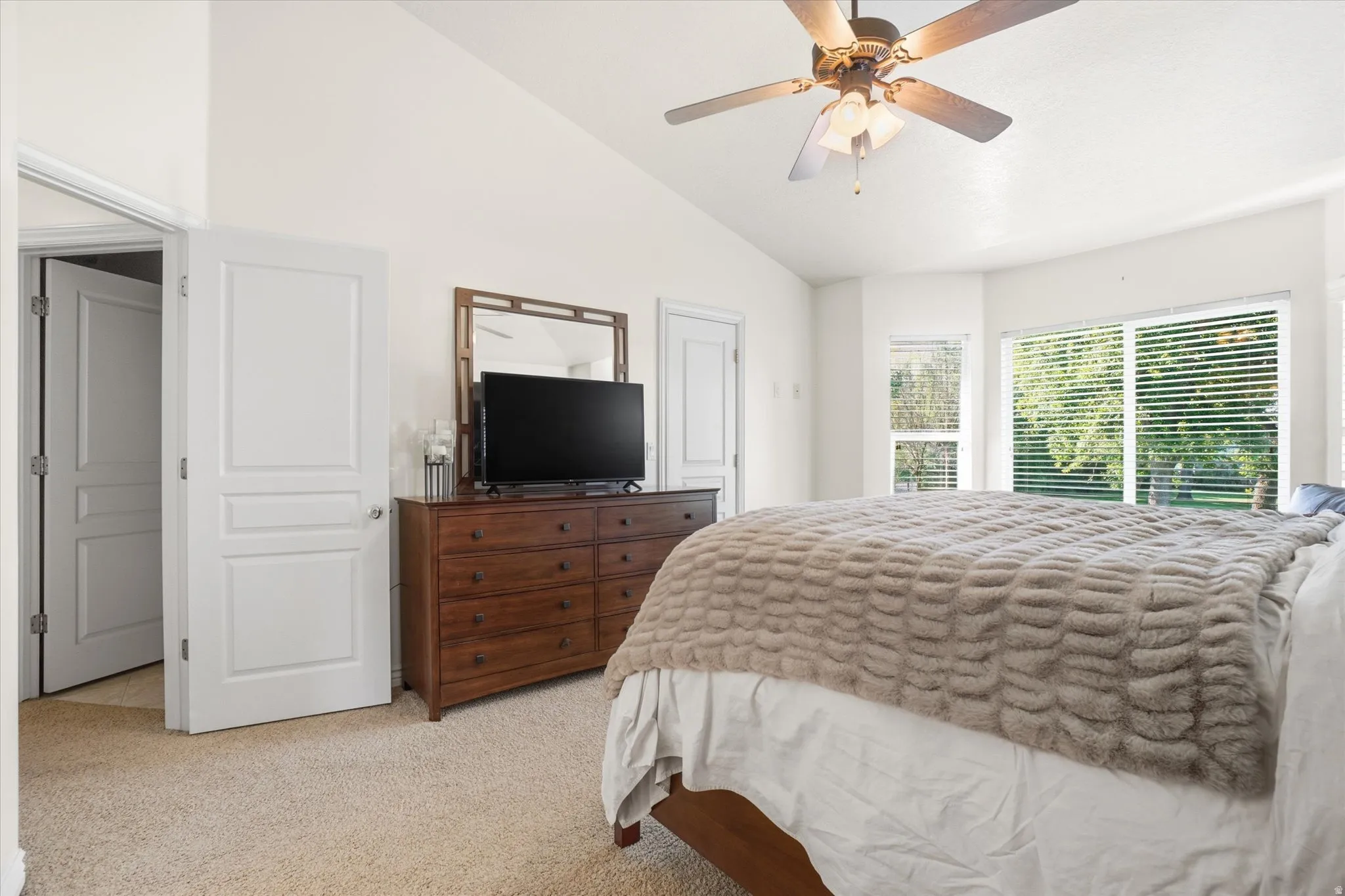 Vaulted ceiling bedroom featuring ample natural light from multiple windows, a ceiling fan, and light-toned carpeting