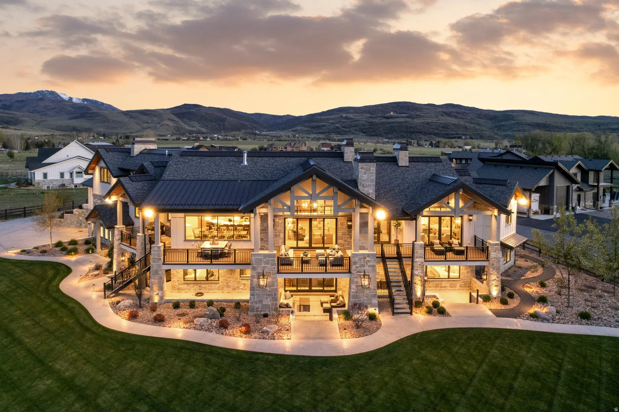 Back of property at dusk with stone siding, a yard, a standing seam roof, a chimney, and a balcony
