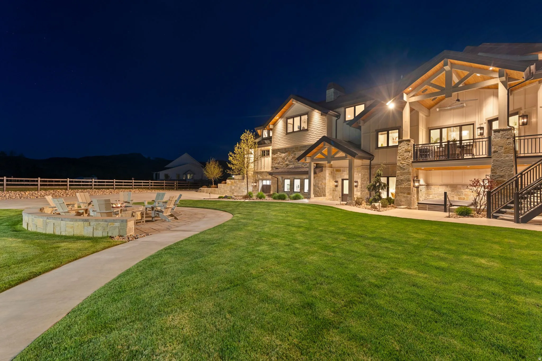 Back of house at night with stone siding, a balcony, a ceiling fan, an outdoor fire pit, and a chimney