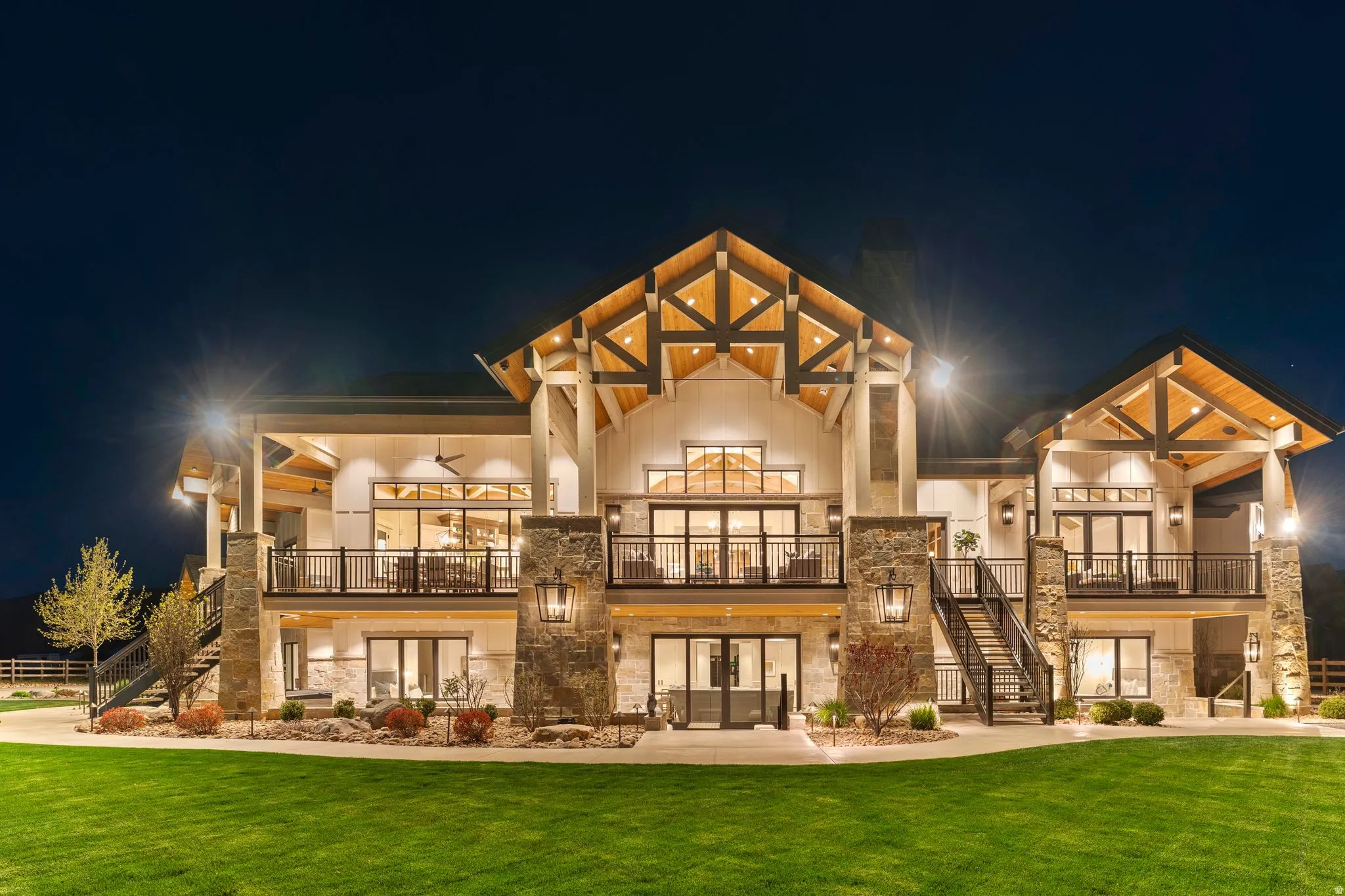 Back of house at twilight featuring stone siding, french doors, a lawn, and a balcony