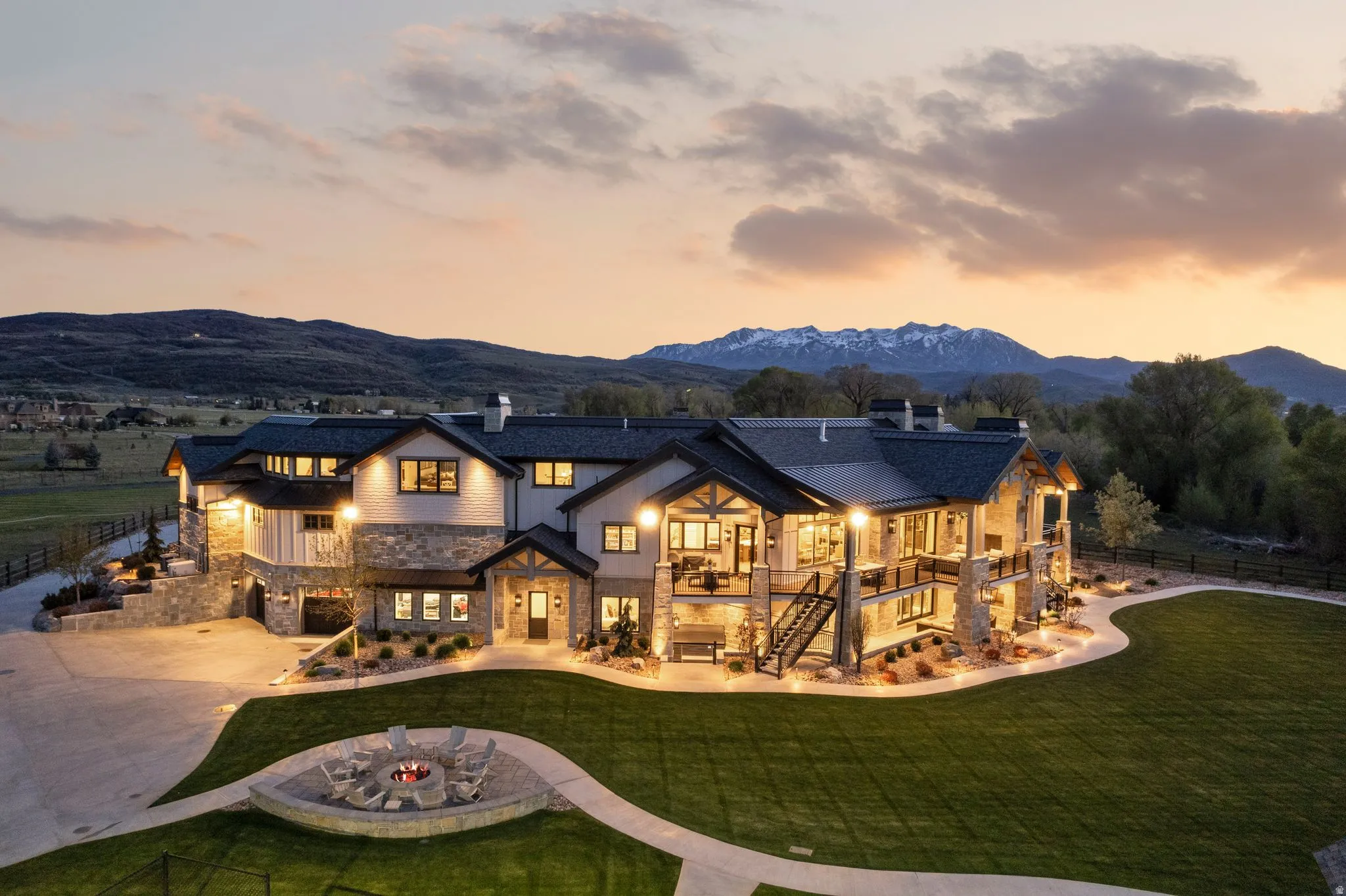 Back of property at dusk featuring a chimney, stone siding, a garage, concrete driveway, and a mountain view