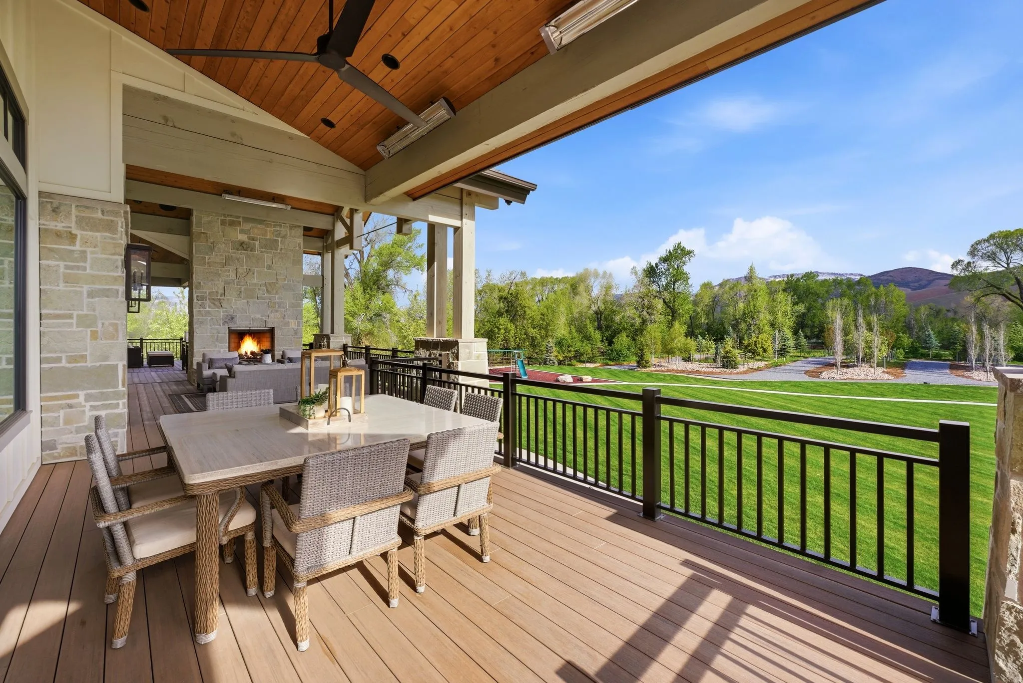 Wooden terrace featuring outdoor dining area, a lawn, an outdoor stone fireplace, and a mountain view