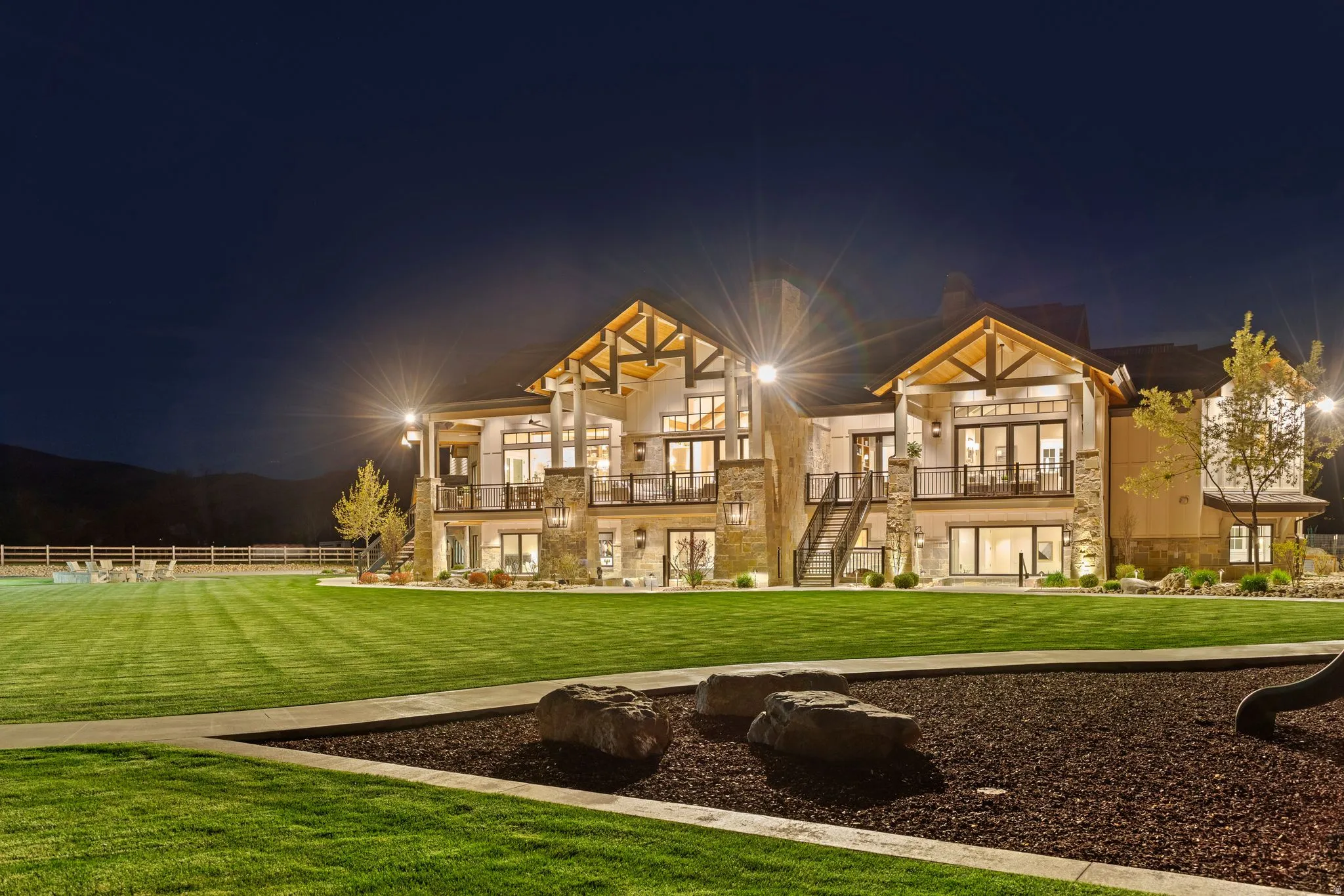 Back of house at night with a lawn, stone siding, and a balcony
