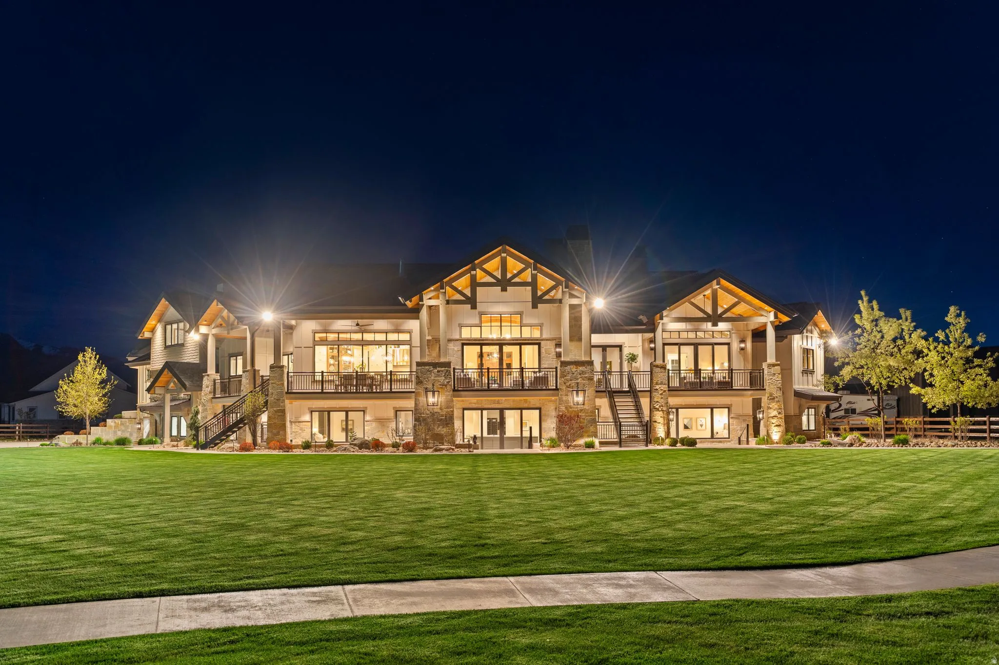 Back of house at night with a balcony, stone siding, and stucco siding