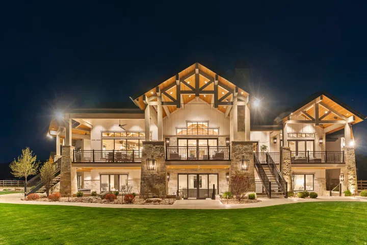 Back of house at twilight featuring stone siding, french doors, a lawn, and a balcony