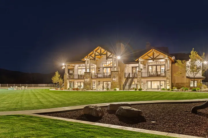 Back of house at night with a lawn, stone siding, and a balcony