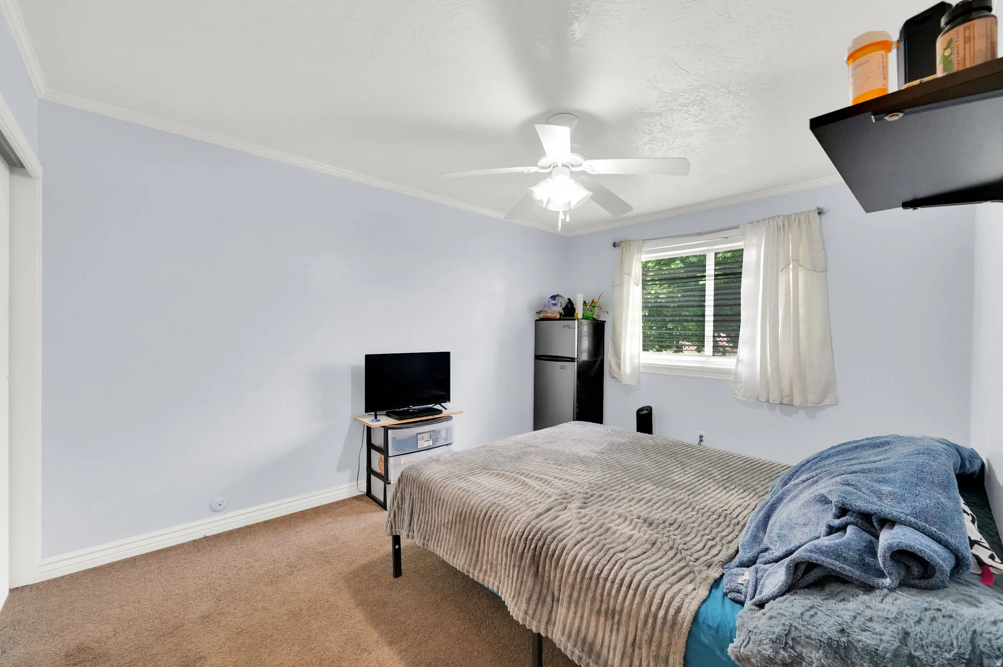 Carpeted bedroom featuring freestanding refrigerator, crown molding, and a ceiling fan