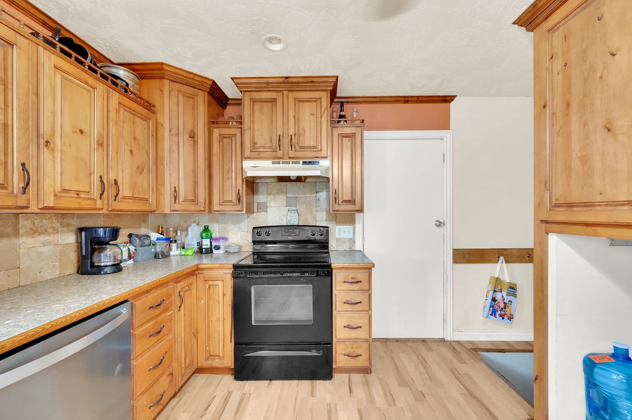 Kitchen featuring electric range, tasteful backsplash, light countertops, stainless steel dishwasher, and light wood-type flooring