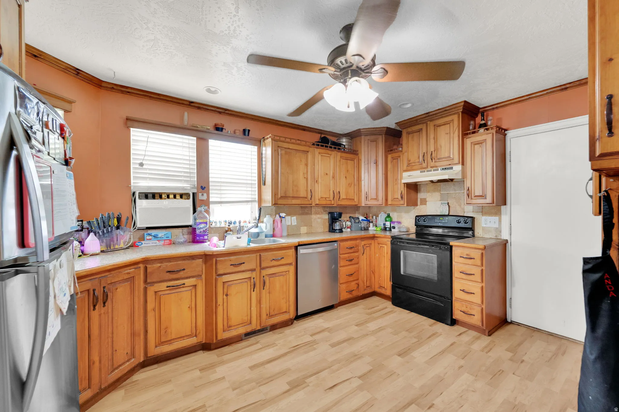Kitchen with light countertops, stainless steel appliances, ornamental molding, ceiling fan, and light wood-style floors