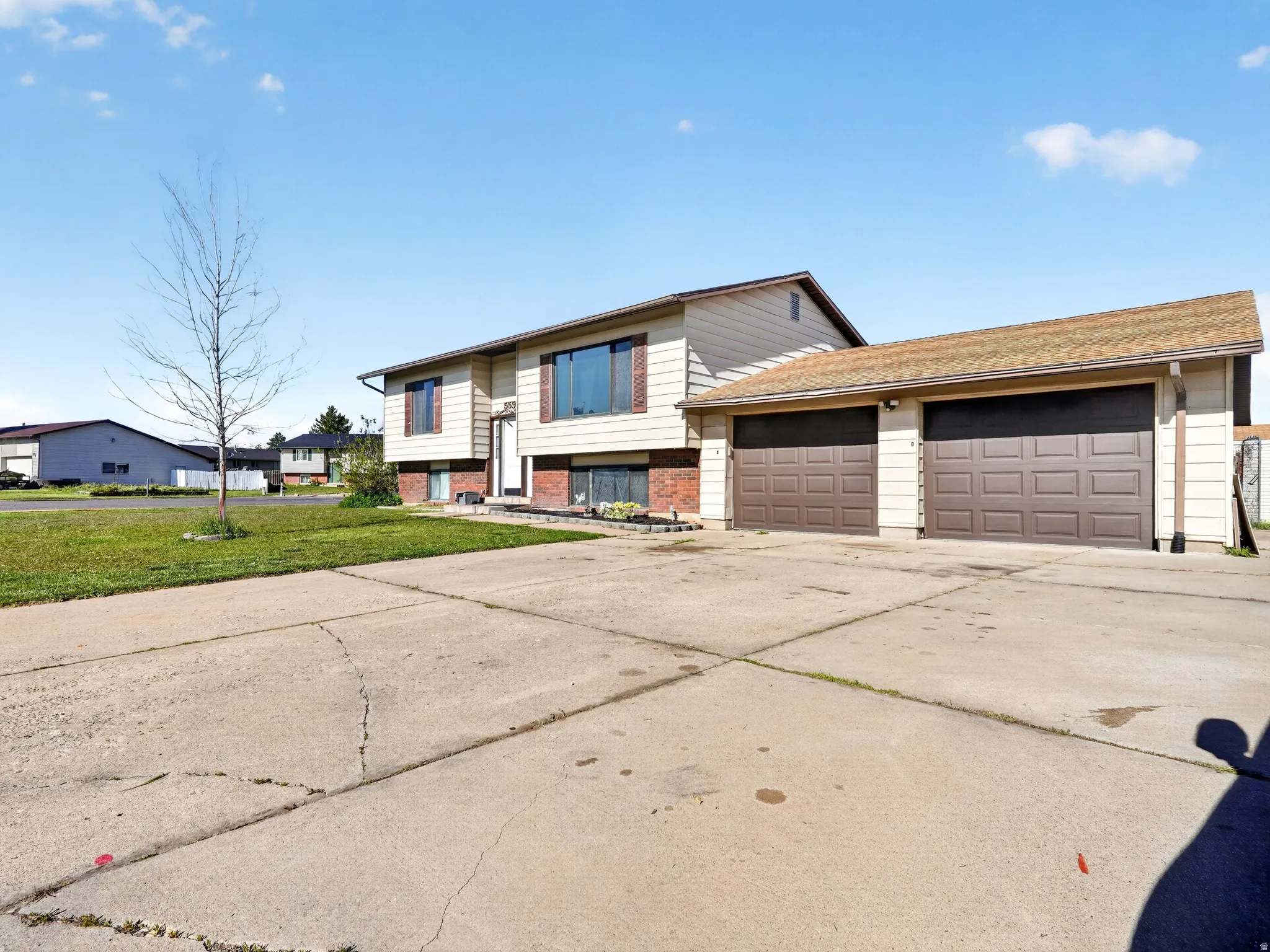 Split foyer home with driveway, brick siding, an attached garage, and a front lawn