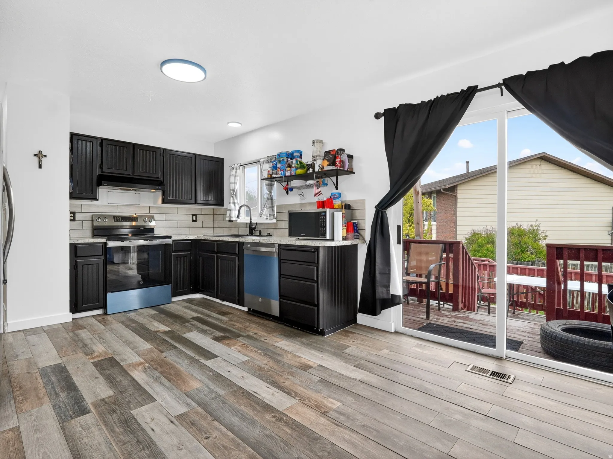 Kitchen with stainless steel appliances, backsplash, dark cabinets, and light wood-type flooring