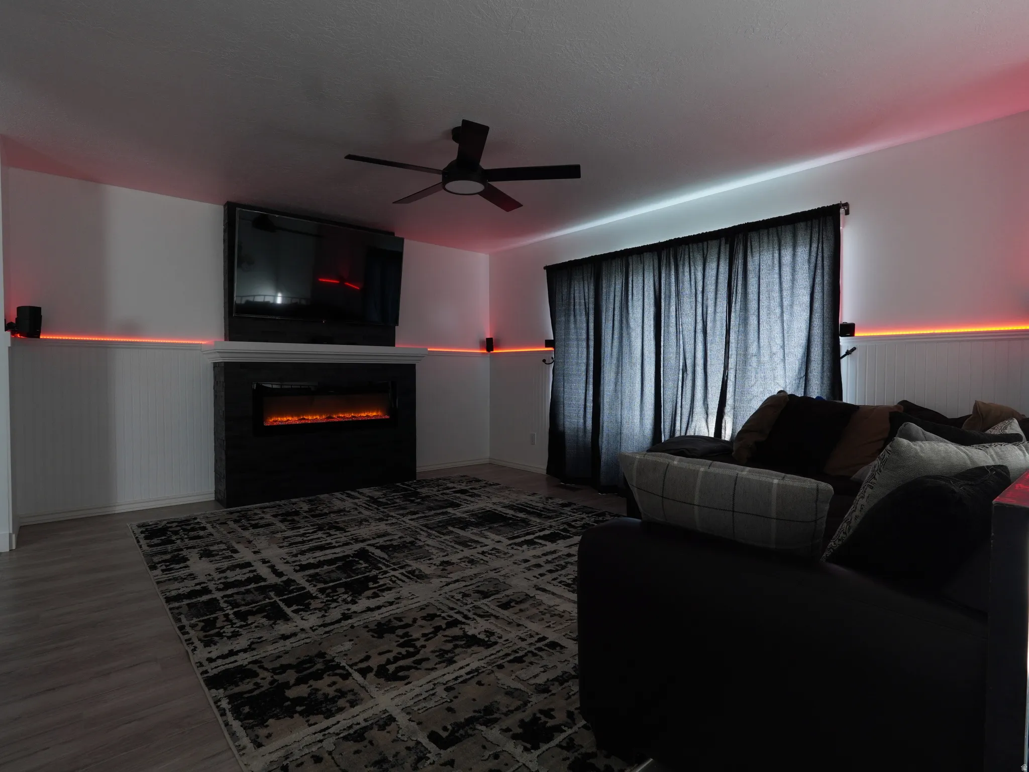Living room featuring wainscoting, ceiling fan, a glass covered fireplace, wood finished floors, and wooden walls