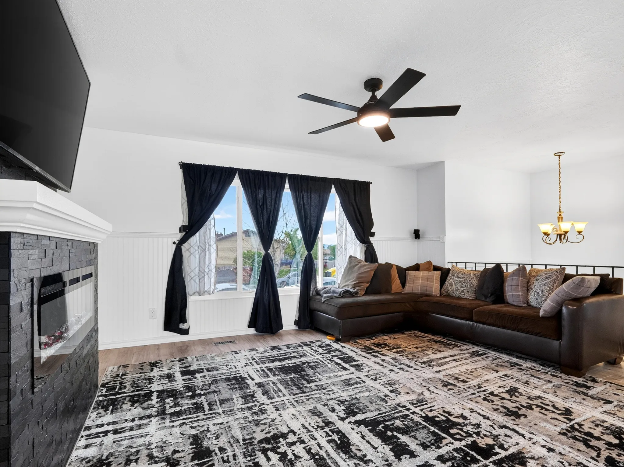 Living area featuring wainscoting, hanging lights, wood finished floors, a ceiling fan, and a brick fireplace