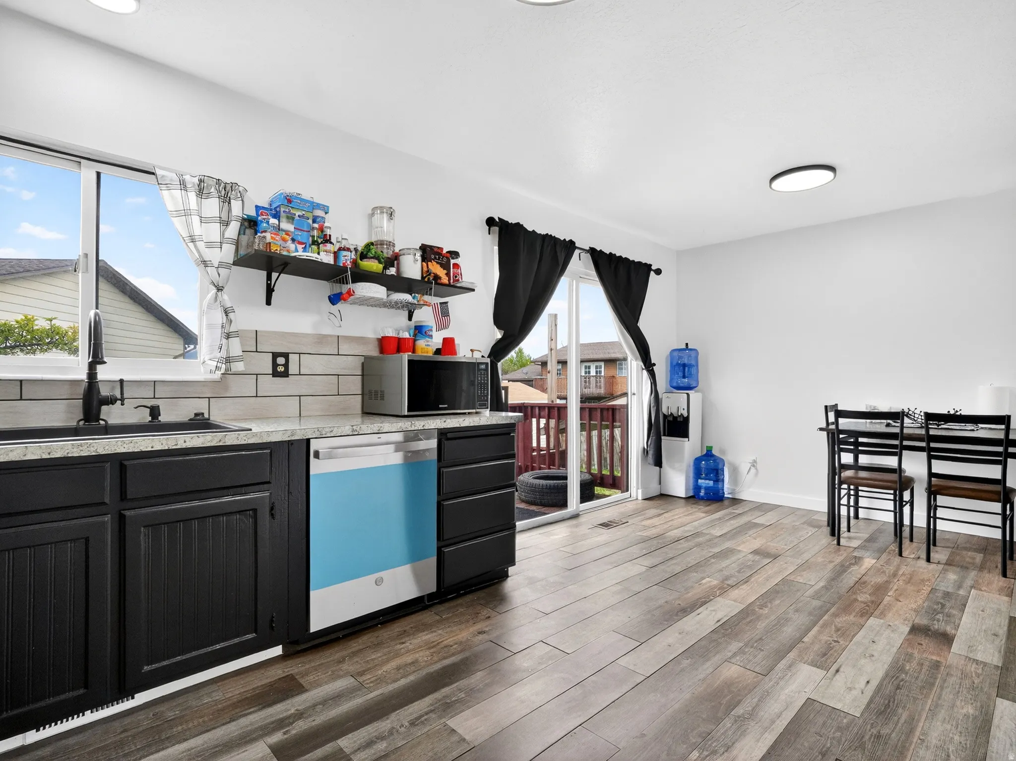 Kitchen featuring dishwasher, decorative backsplash, stainless steel microwave, open shelves, and dark wood-type flooring