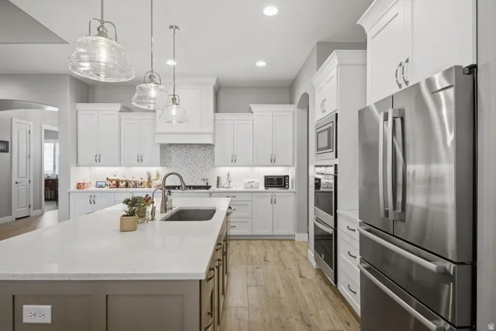 Kitchen featuring stainless steel appliances, arched walkways, light wood-style floors, a center island with sink, and light stone counters