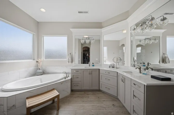 Full bathroom featuring double vanity, healthy amount of natural light, a garden tub, and light wood finished floors