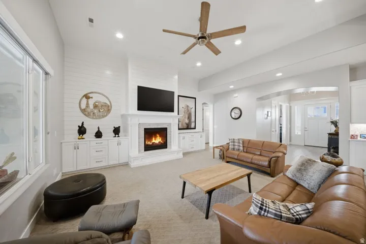 Living area featuring ceiling fan, light colored carpet, a lit fireplace, arched walkways, and recessed lighting